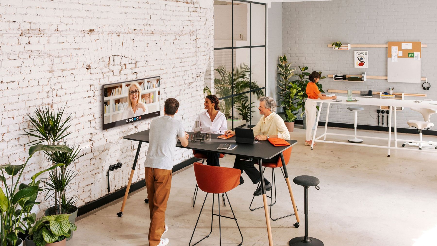 An einem schwarzen Stehtisch befinden sich drei Personen, die an einer Videokonferenz teilnehmen.