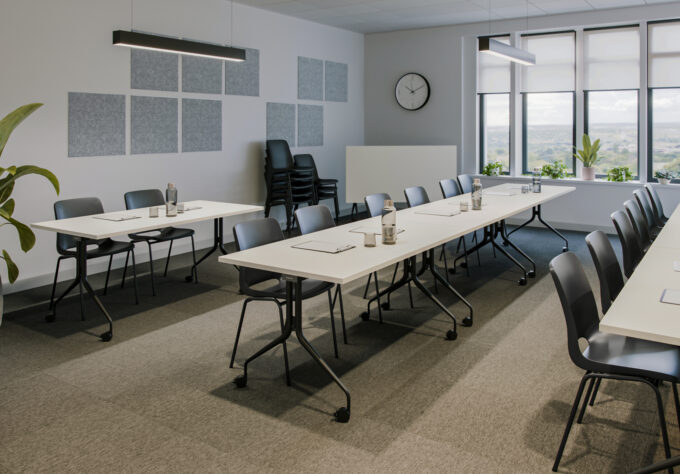 A modern seminar room equipped with white swivel tables, black stackable chairs, and acoustic panels on the walls.