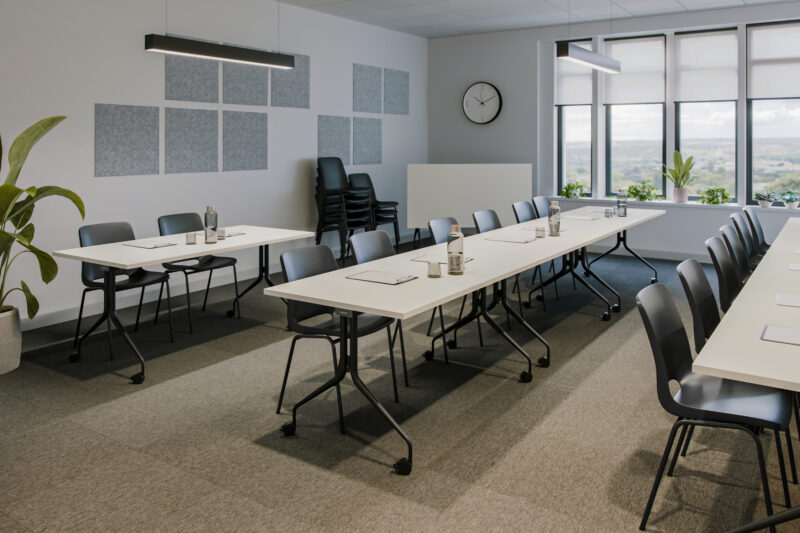A modern seminar room equipped with white swivel tables, black stackable chairs, and acoustic panels on the walls.