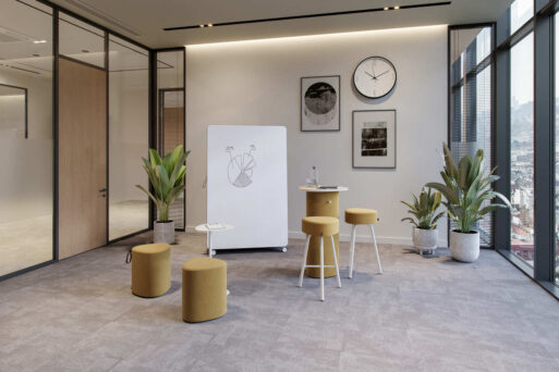 neudoerfler Create Box in hellen Farbtönen mit Stehtisch, Sitzmöbeln und Whiteboard für kreativen Austausch im Büro.