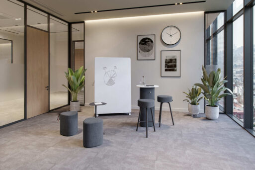 neudoerfler Create Box in dunklen Farbtönen mit Stehtisch, Sitzmöbeln und Whiteboard für kreativen Austausch im Büro.