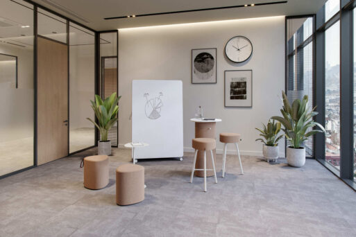 neudoerfler Create Box in hellen Farbtönen mit Stehtisch, Sitzmöbeln und Whiteboard für kreativen Austausch im Büro.