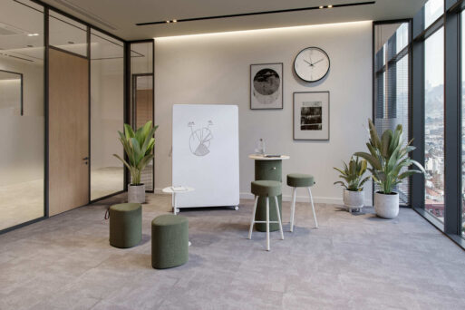 neudoerfler Create Box in grünen Farbtönen mit Stehtisch, Sitzmöbeln und Whiteboard für kreativen Austausch im Büro.