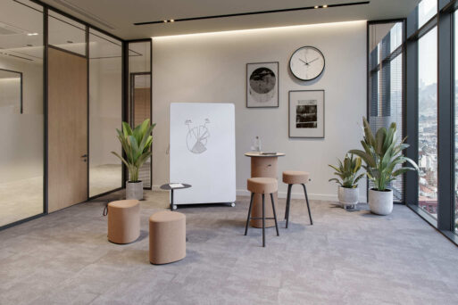 neudoerfler Create Box in warmen Holztönen mit Stehtisch, Sitzmöbeln und Whiteboard für kreativen Austausch im Büro.